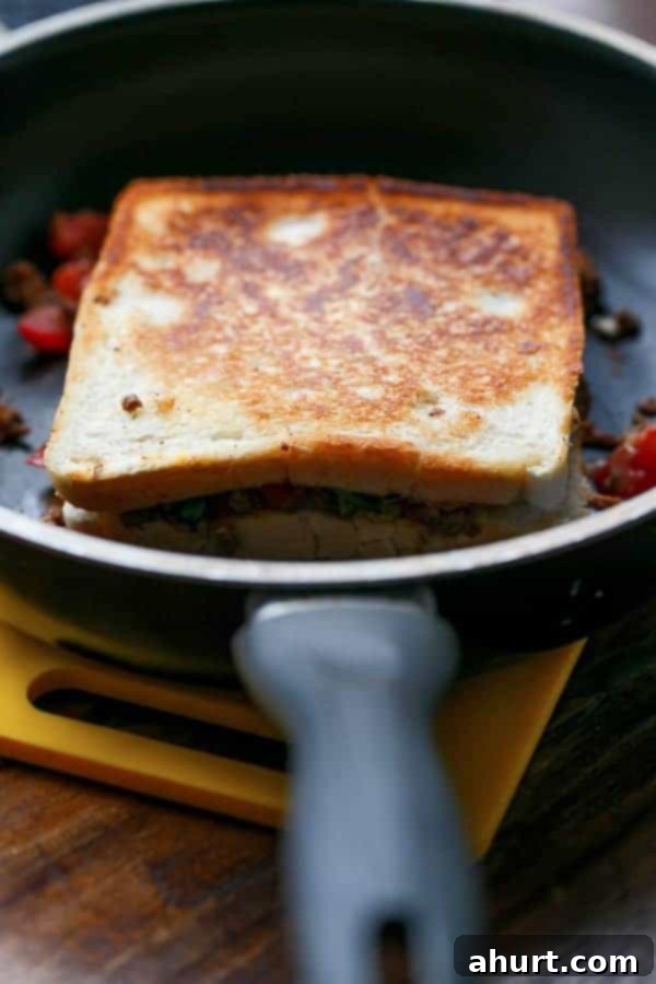 Loaded Taco Grilled Cheese sandwich being toasted on a hot pan, showing a golden crust forming.
