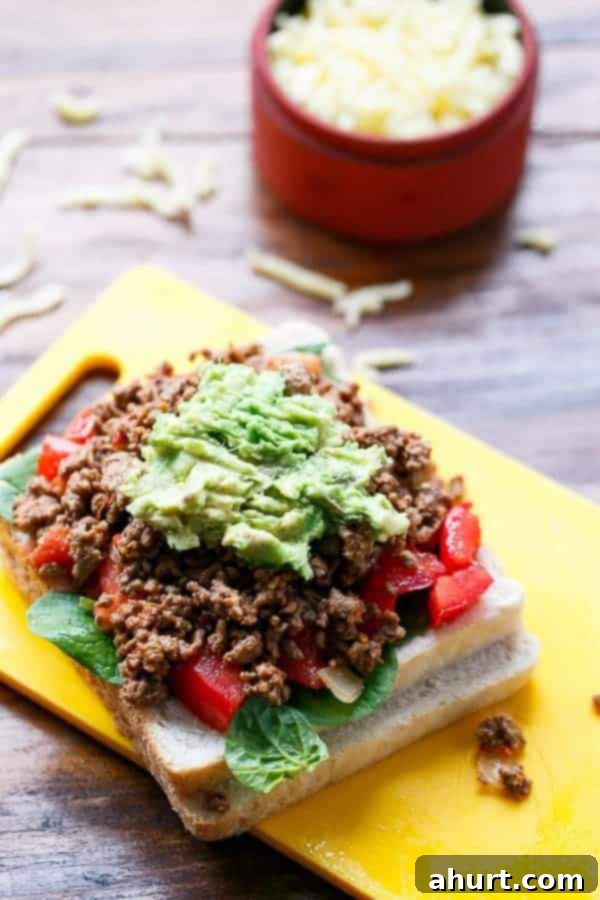 Assembling of Loaded Taco Grilled Cheese sandwich, with layers of mince, cheese, and vegetables on bread.