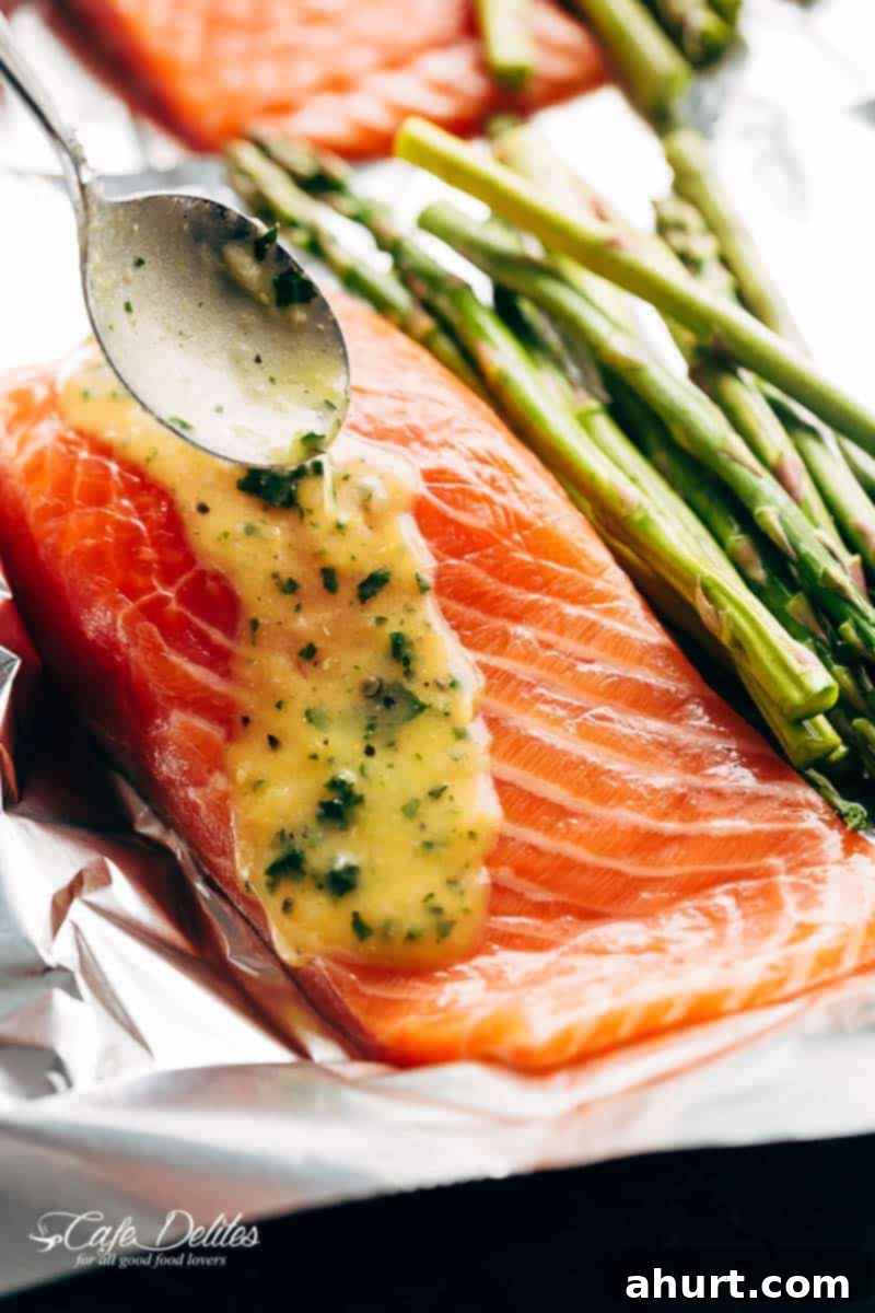 Zesty Lemon Parmesan Salmon and Asparagus Foil Packets 3 Raw salmon fillets and asparagus spears being drizzled with a rich lemon garlic butter sauce before sealing in foil packets.