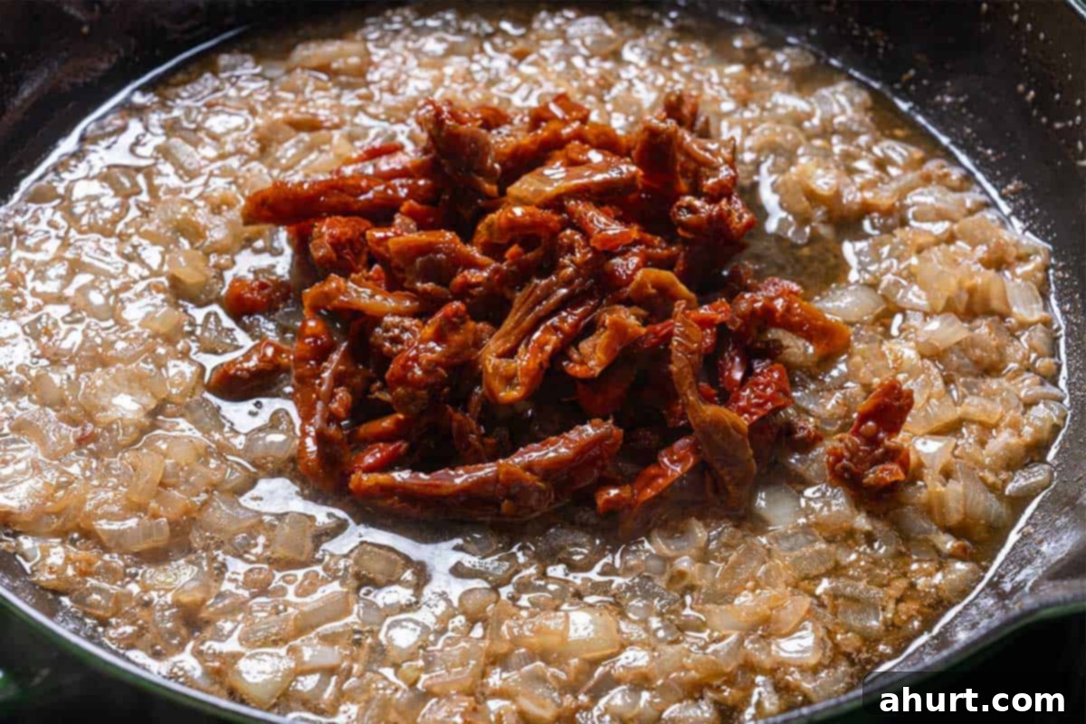 Velvety Tuscan Garlic Butter Salmon 6 Image of sun-dried tomatoes being added to the sautéed onions and garlic in butter, releasing their rich flavors.