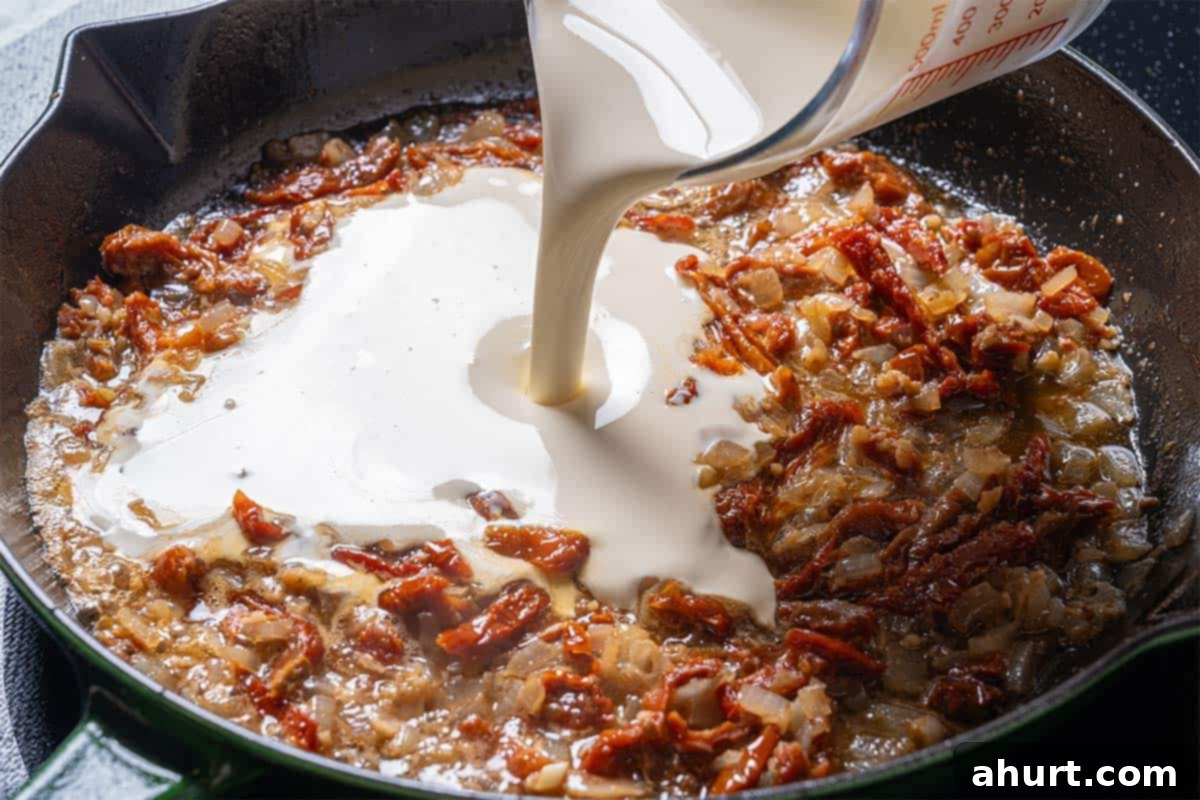 Velvety Tuscan Garlic Butter Salmon 7 An image of half and half or heavy cream being slowly poured into the simmering mixture of onions, garlic, and sun-dried tomatoes, creating the creamy sauce base.
