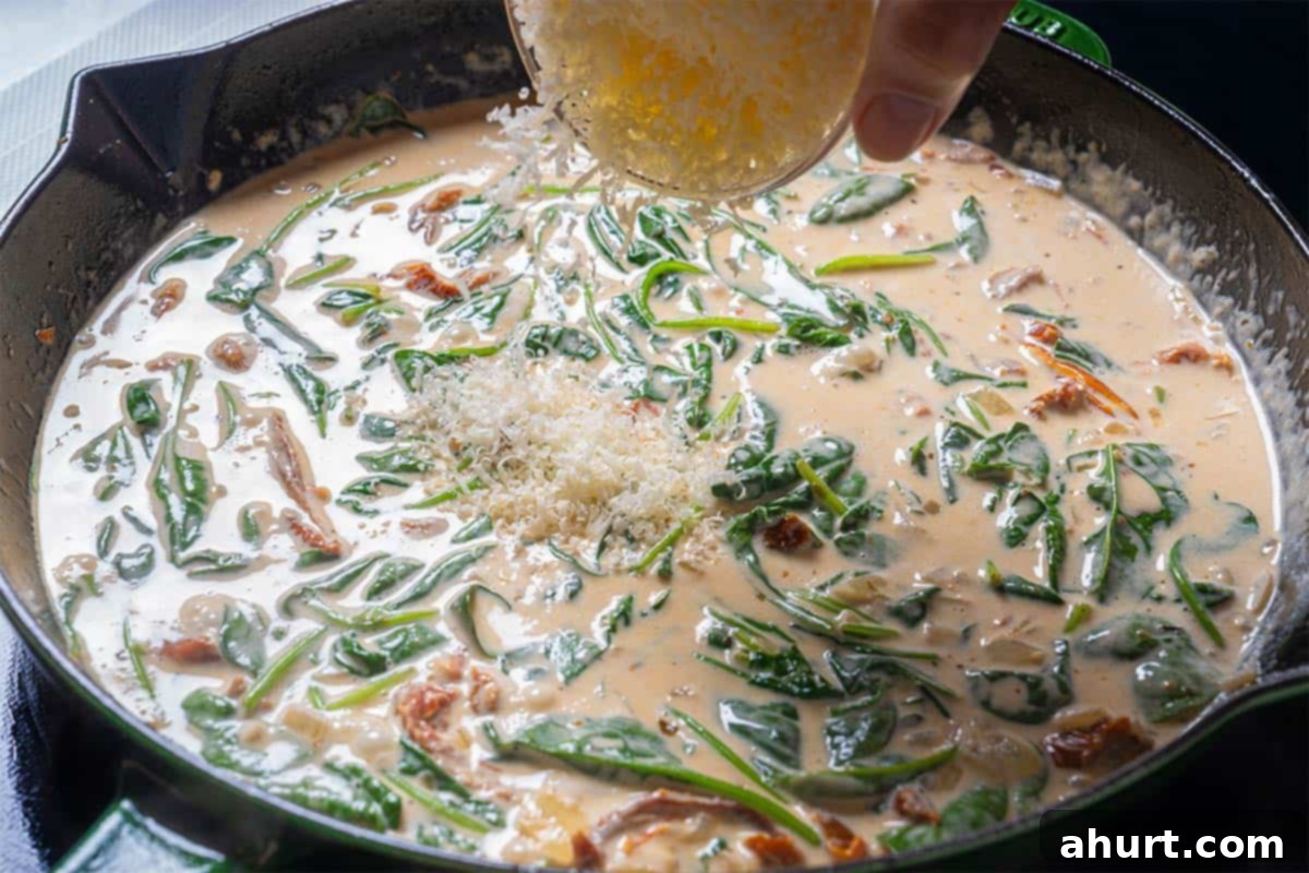 Velvety Tuscan Garlic Butter Salmon 8 Image of fresh spinach and grated Parmesan cheese being added to the rich, creamy sauce, beginning to wilt and melt.