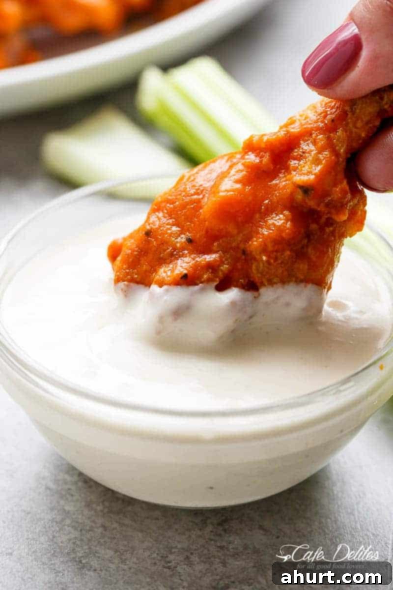 Golden Crisp Baked Buffalo Wings 12 An image of a chicken wing covered in buffalo sauce being dipped into blue cheese sauce.