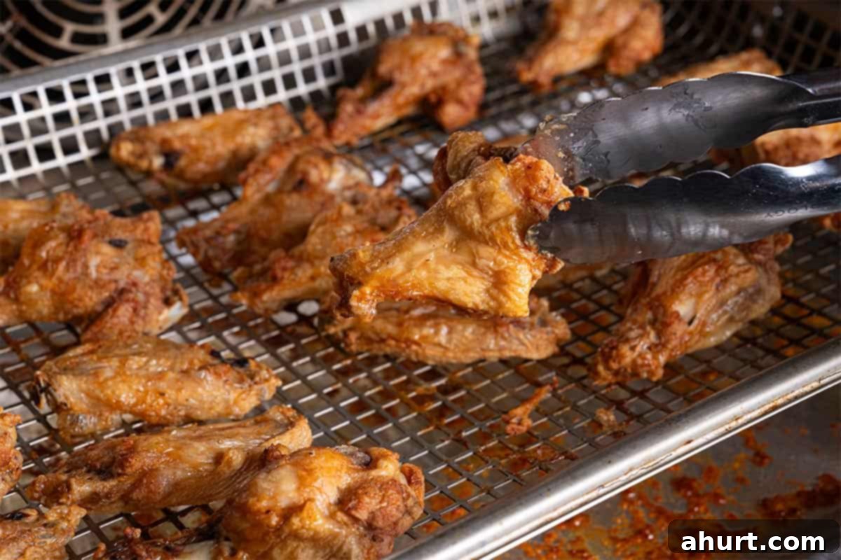 Golden Crisp Baked Buffalo Wings 8 Partially baked chicken wings being flipped on the wire rack to ensure even crisping.