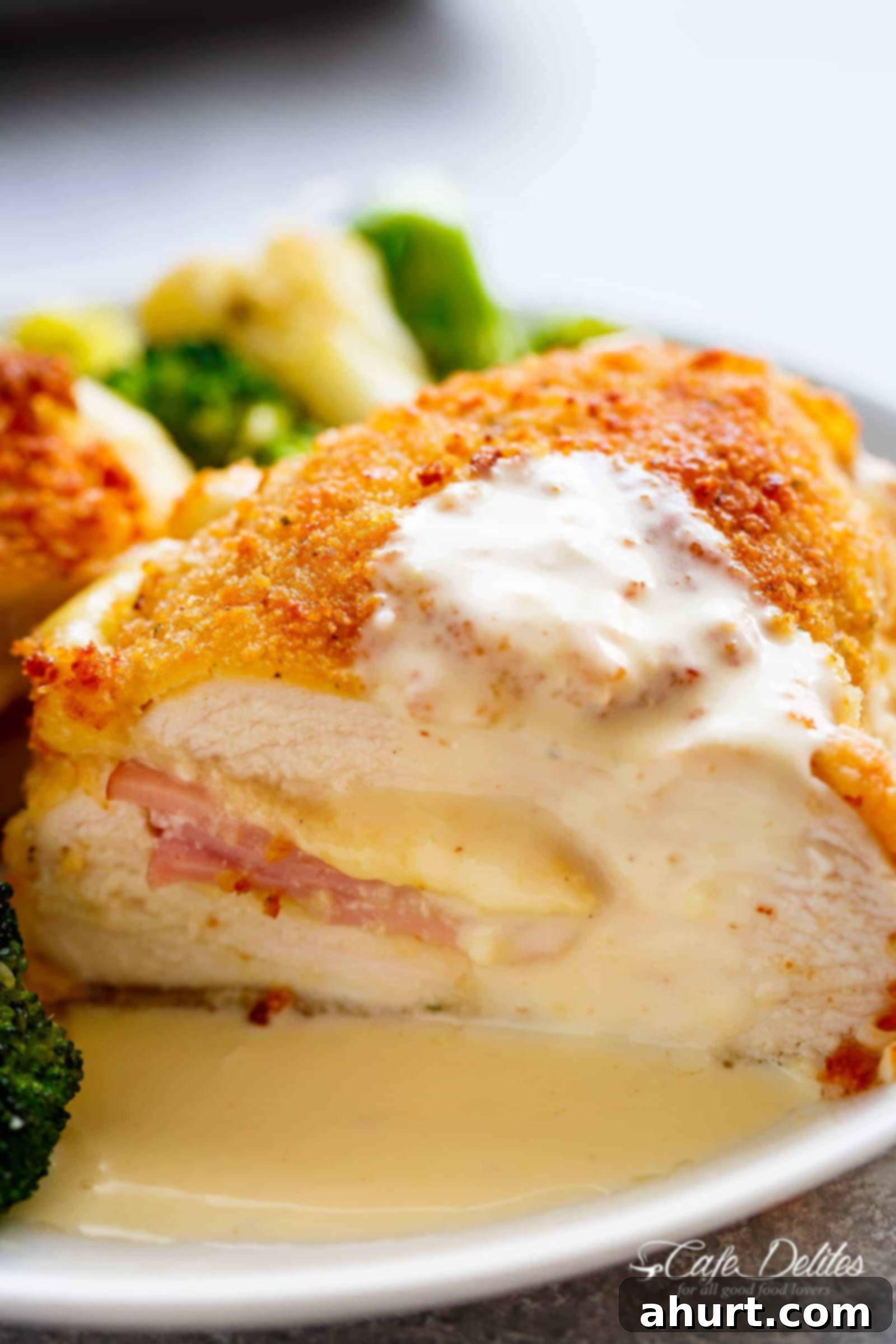 Side view of Crispy crumbed chicken breasts filled with Dijon mustard, Swiss cheese and ham, baked with vegetables and served with an incredible Dijon Cream Sauce