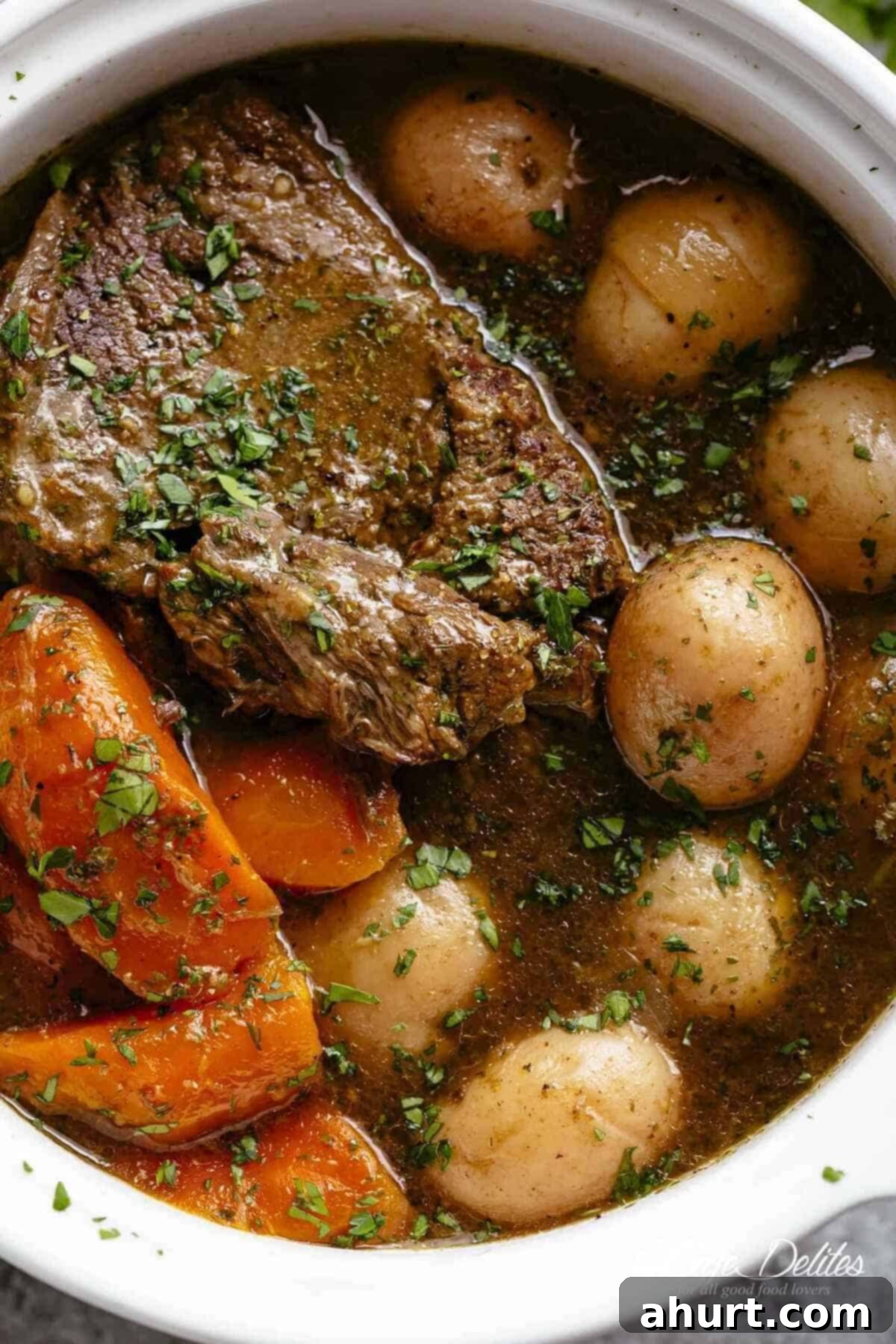Melt In Your Mouth Pot Roast 2 A close-up image of a tender piece of beef chuck, cooked in its own juices alongside potatoes and carrots.