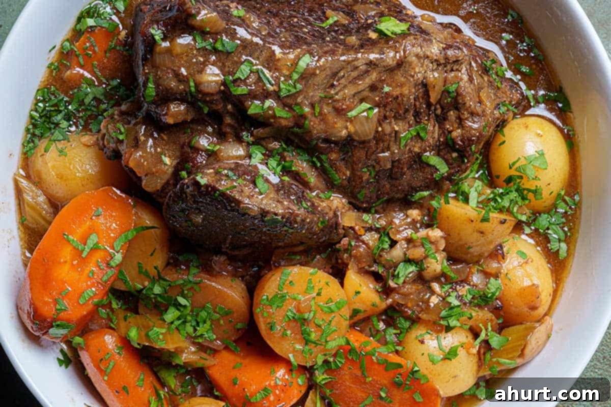 Melt In Your Mouth Pot Roast 9 An image of the finished pot roast served on a round white plate, accompanied by potatoes and carrots, and sprinkled with fresh parsley.