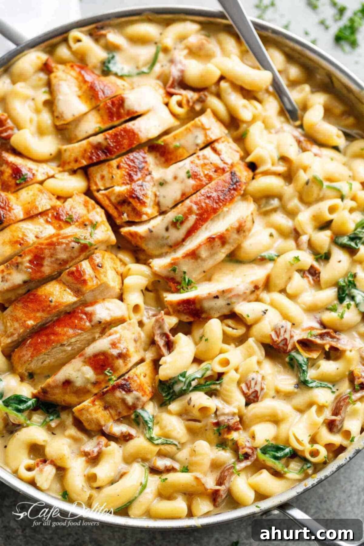 Hearty Tuscan Chicken Skillet Mac 2 Tuscan chicken sliced, on top of a bed of creamy pasta with sundered tomatoes and spinach with Fresh herbs sprinkled on top.