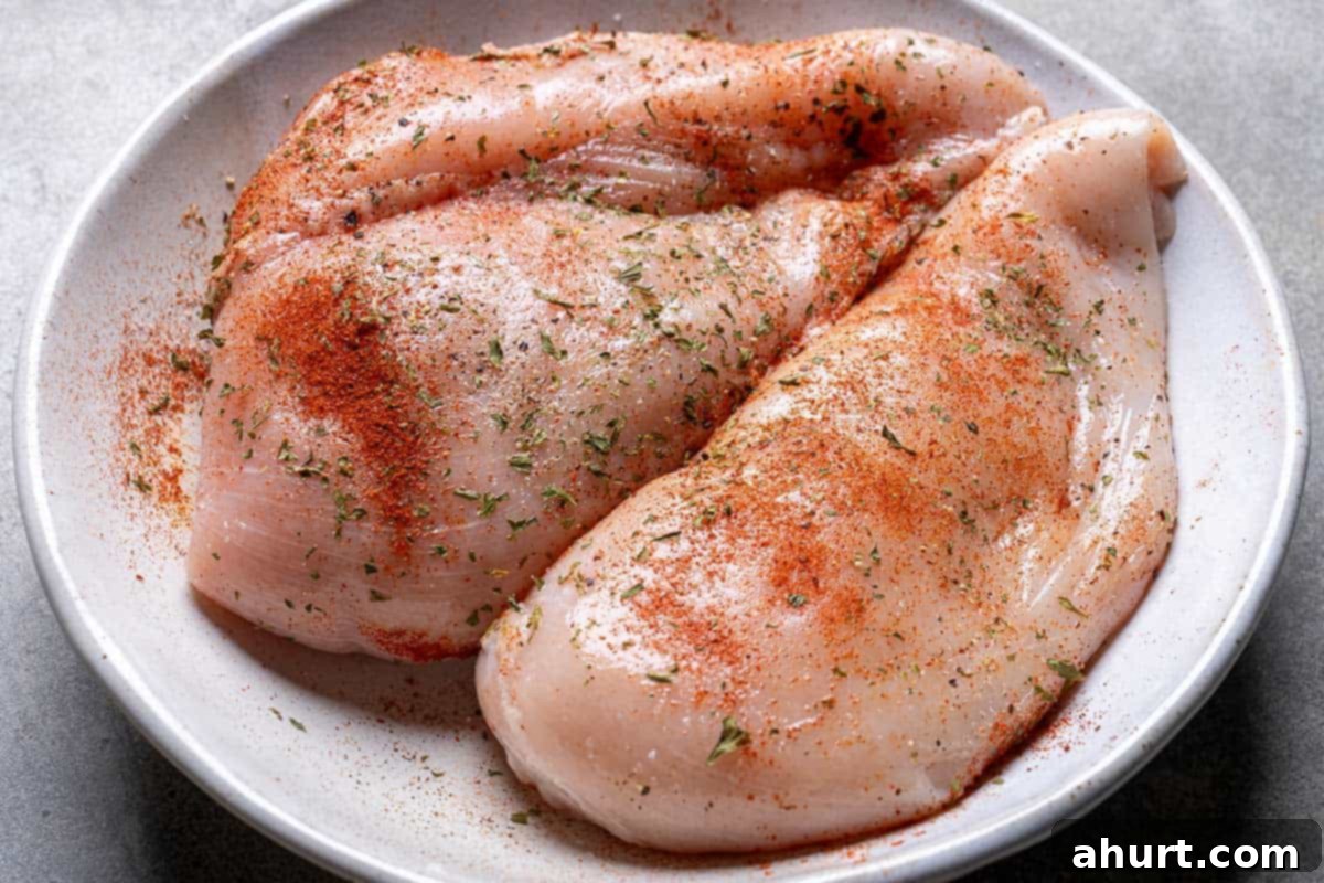 Hearty Tuscan Chicken Skillet Mac 4 Chicken breasts in a white bowl, evenly coated with salt, pepper, paprika, dried parsley, and 2 teaspoons of oil, ready for searing.