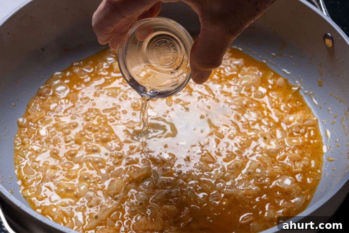 Hearty Tuscan Chicken Skillet Mac 6 Wine being poured into the pan, enhancing the flavors of the sautéed aromatics as they cook.