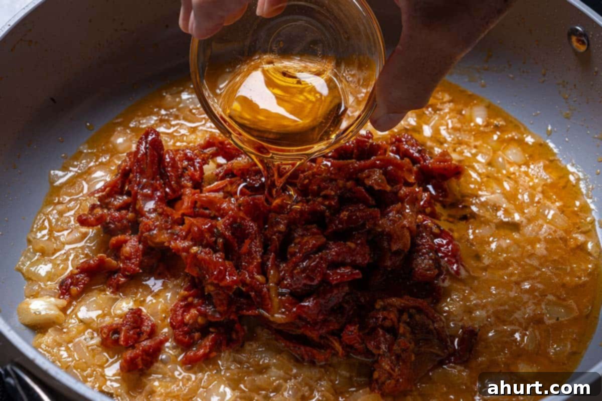 Hearty Tuscan Chicken Skillet Mac 7 Sun-dried tomatoes and their infused oil being added to the pan, releasing rich, tangy flavors into the dish.