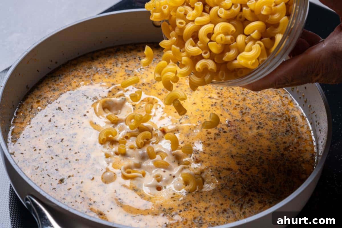 Hearty Tuscan Chicken Skillet Mac 9 Dry macaroni being poured into the creamy sauce, ready to cook until perfectly 'al dente.