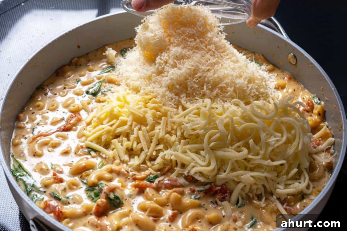 Hearty Tuscan Chicken Skillet Mac 10 Cheese being stirred into the pot of macaroni and sauce, creating a creamy, luscious texture.