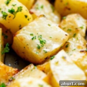 Golden Crispy Garlic Potatoes 9 Close up image of Crispy garlic roasted potatoes sprinkled with fresh green herbs on a baking tray.