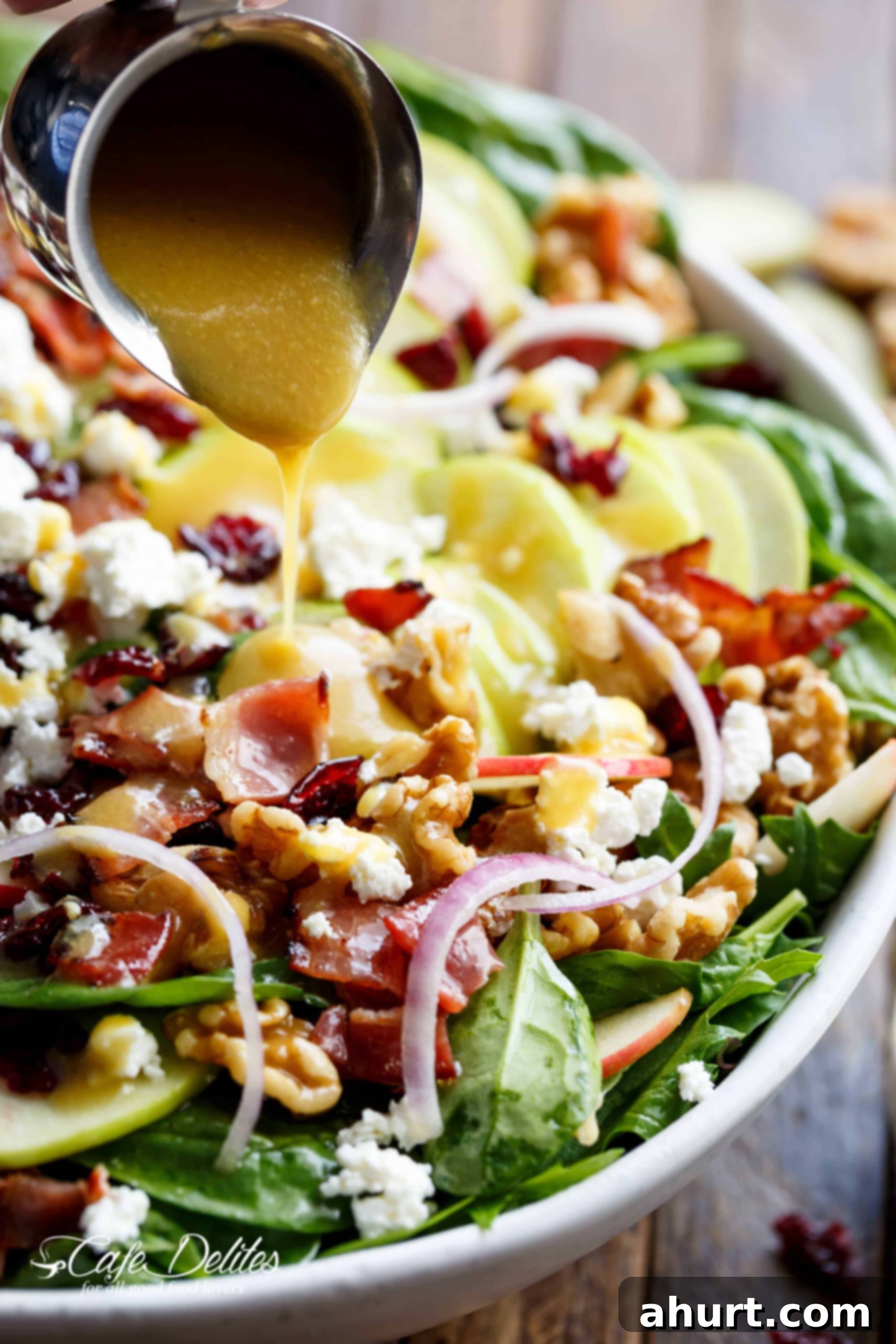 Honey Dijon dressing being elegantly poured over a fresh Honey Dijon Apple Bacon Cranberry Salad, highlighting the glistening texture of the dressing on the vibrant ingredients.