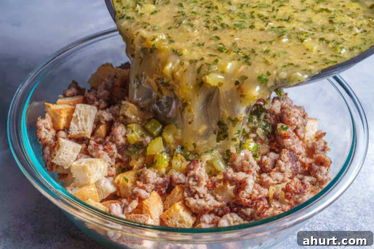 Irresistible Sausage Stuffing 7 Step 4: The image shows broth being poured over a mixture of bread cubes, sausage, and vegetables in a transparent bowl.