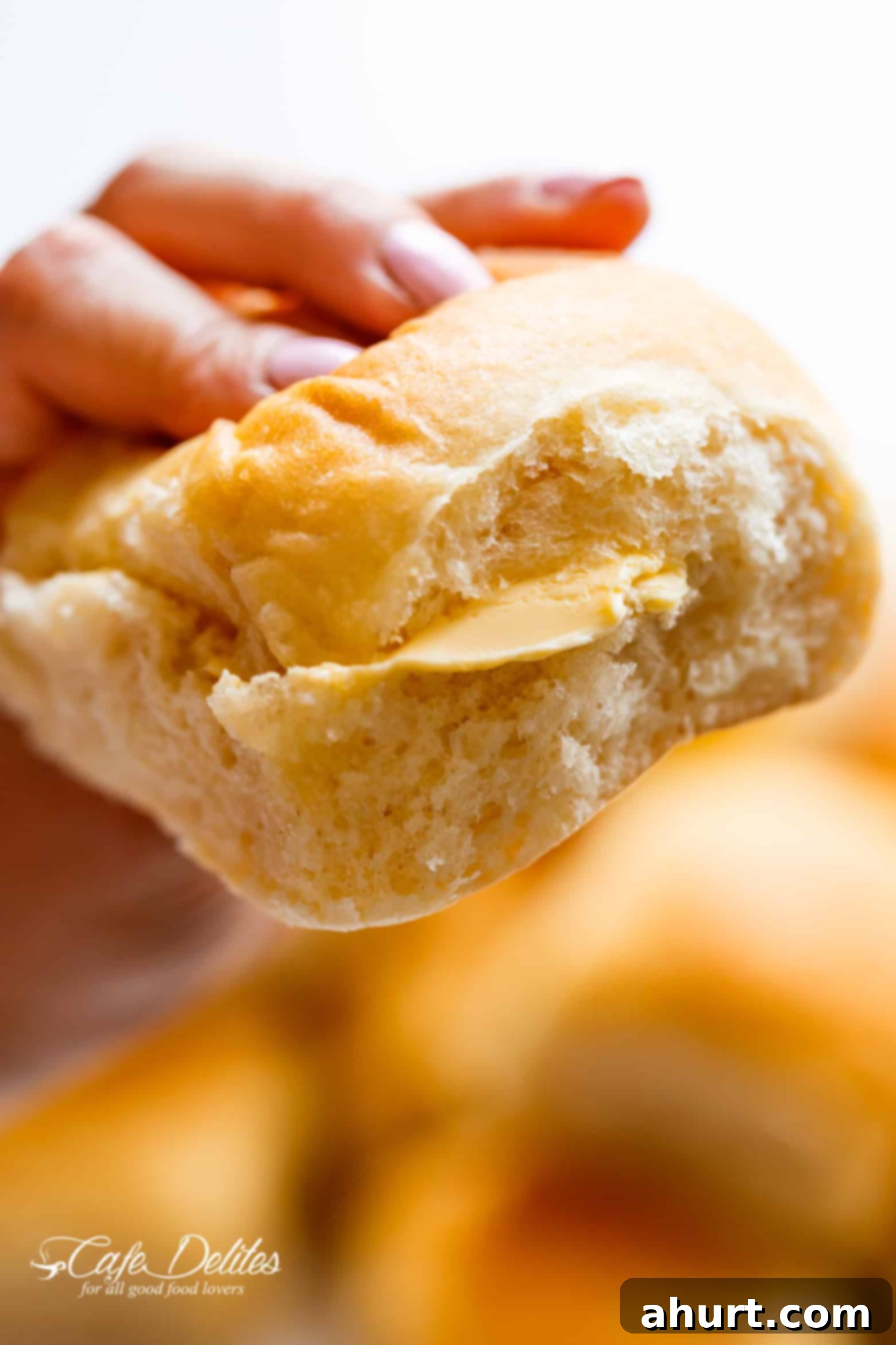 Pillowy Soft Dinner Rolls Hand Kneaded And Egg Free 3 A hand gently tearing apart a warm, soft dinner roll, revealing a luscious slice of butter melting into its fluffy interior.