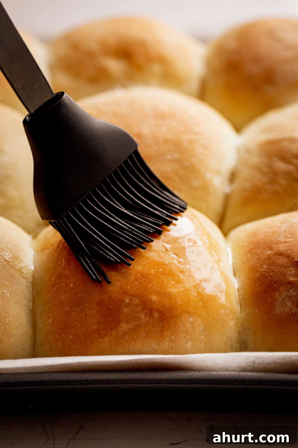 Pillowy Soft Dinner Rolls Hand Kneaded And Egg Free 8 Golden soft dinner rolls being brushed with a light coating of melted butter, fresh out of the oven, enhancing their shine and flavor.