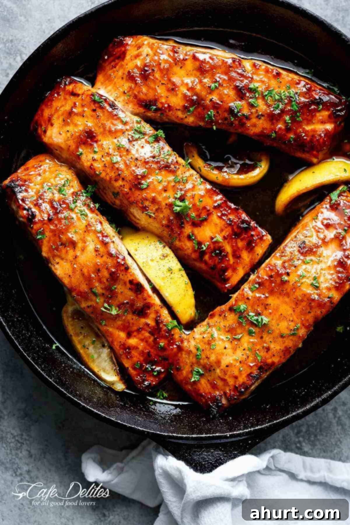 Glazed Honey Garlic Salmon 2 Close-up image of salmon fillets accompanied by lemon in a skillet coated with honey garlic sauce.