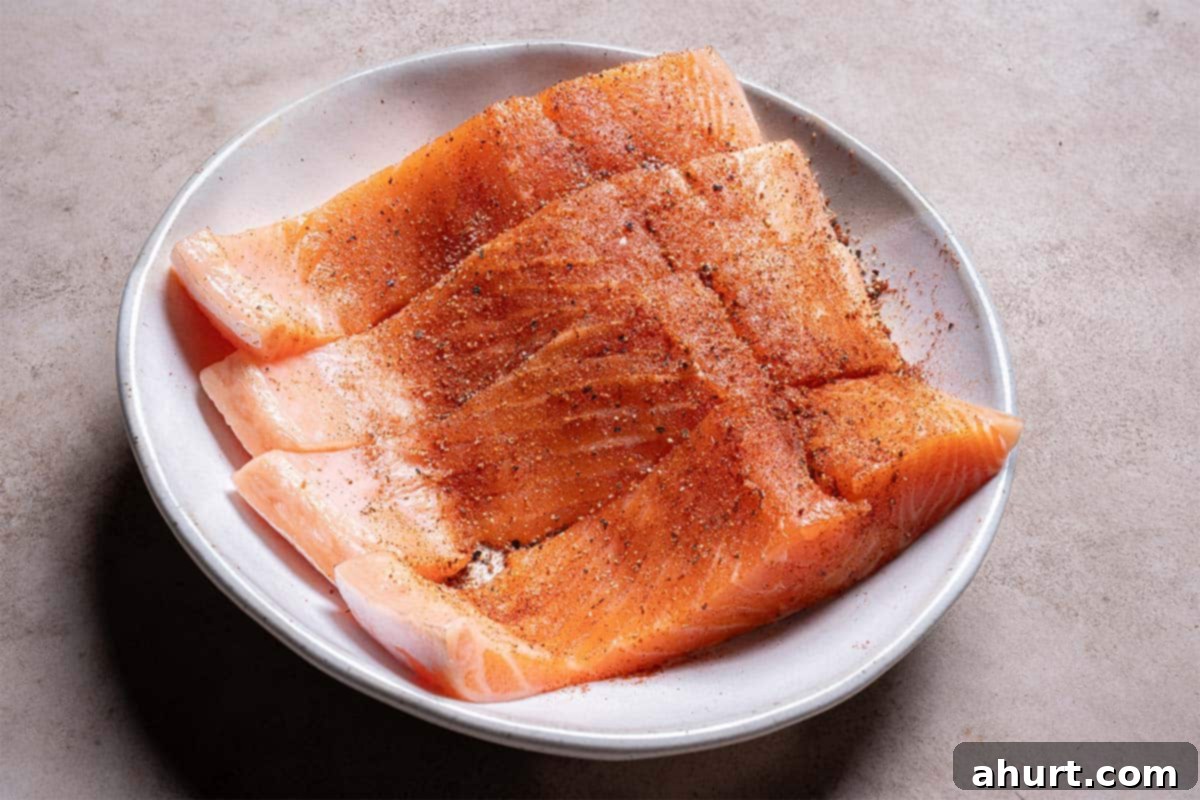 Glazed Honey Garlic Salmon 4 An image depicts four salmon fillets being seasoned in a white bowl while the oven is preheating.