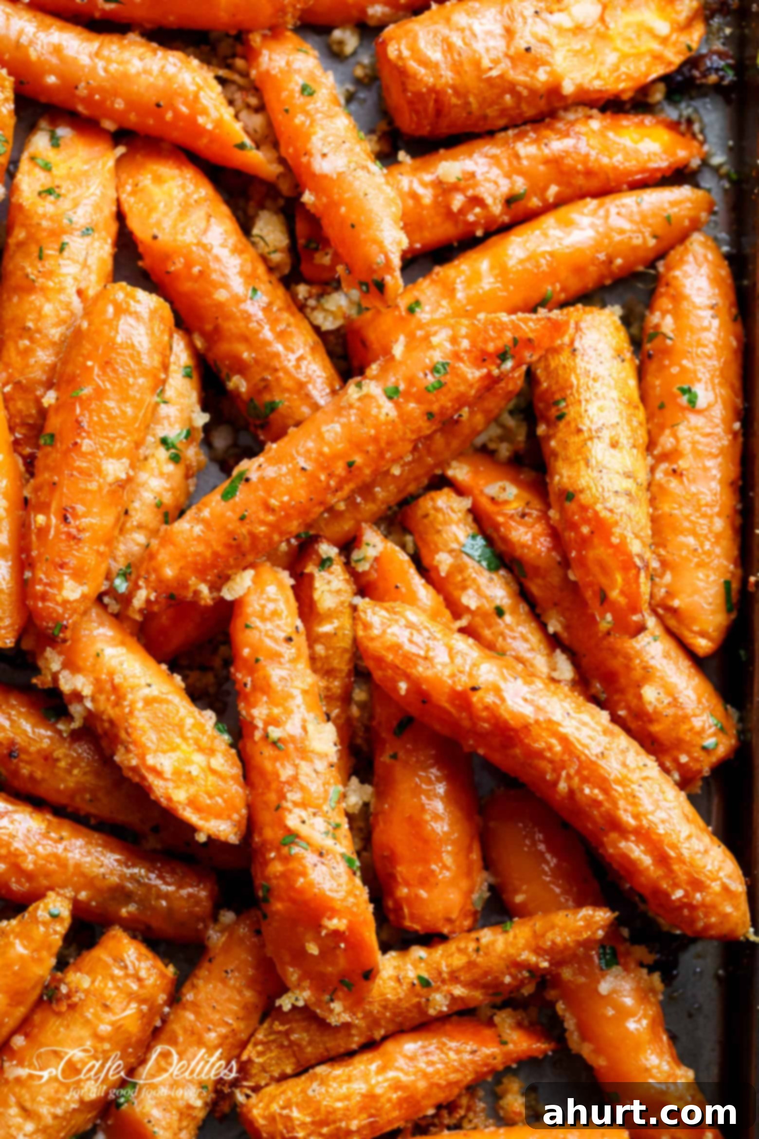 Crispy Parmesan Roasted Carrots 2 This close-up shot image of showcases a tantalizing dish of roasted carrots. Tightly packed together on a baking sheet, the carrots are a vibrant orange, glistening with a delicious glaze. A scattering of herbs, likely parsley, adds a touch of green and hints at a savory flavor profile. The edges of some carrots are slightly caramelized, promising a delightful sweetness and crunch.