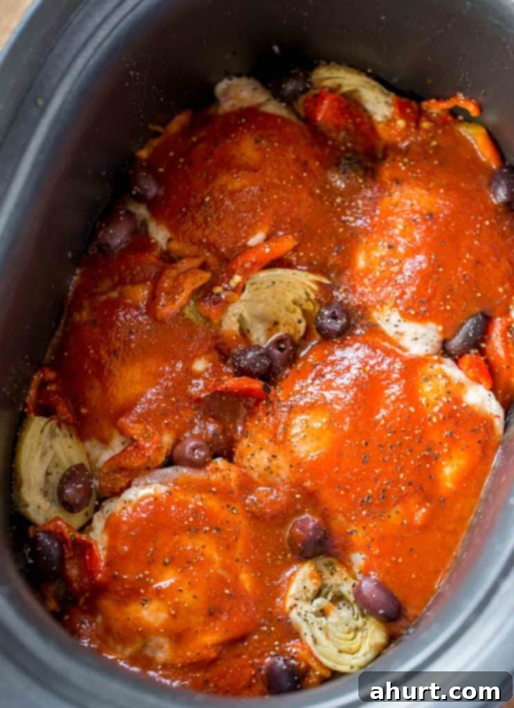 Raw chicken thighs arranged with Mediterranean sauce ingredients in a slow cooker, ready for cooking.