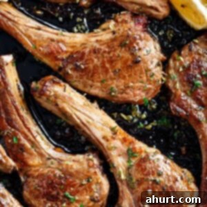 Traditional Greek Lamb Chops 9 cooked lamb chops pieces in a black pan, green herbs sprinkled on top with two lemon wedges to one side.