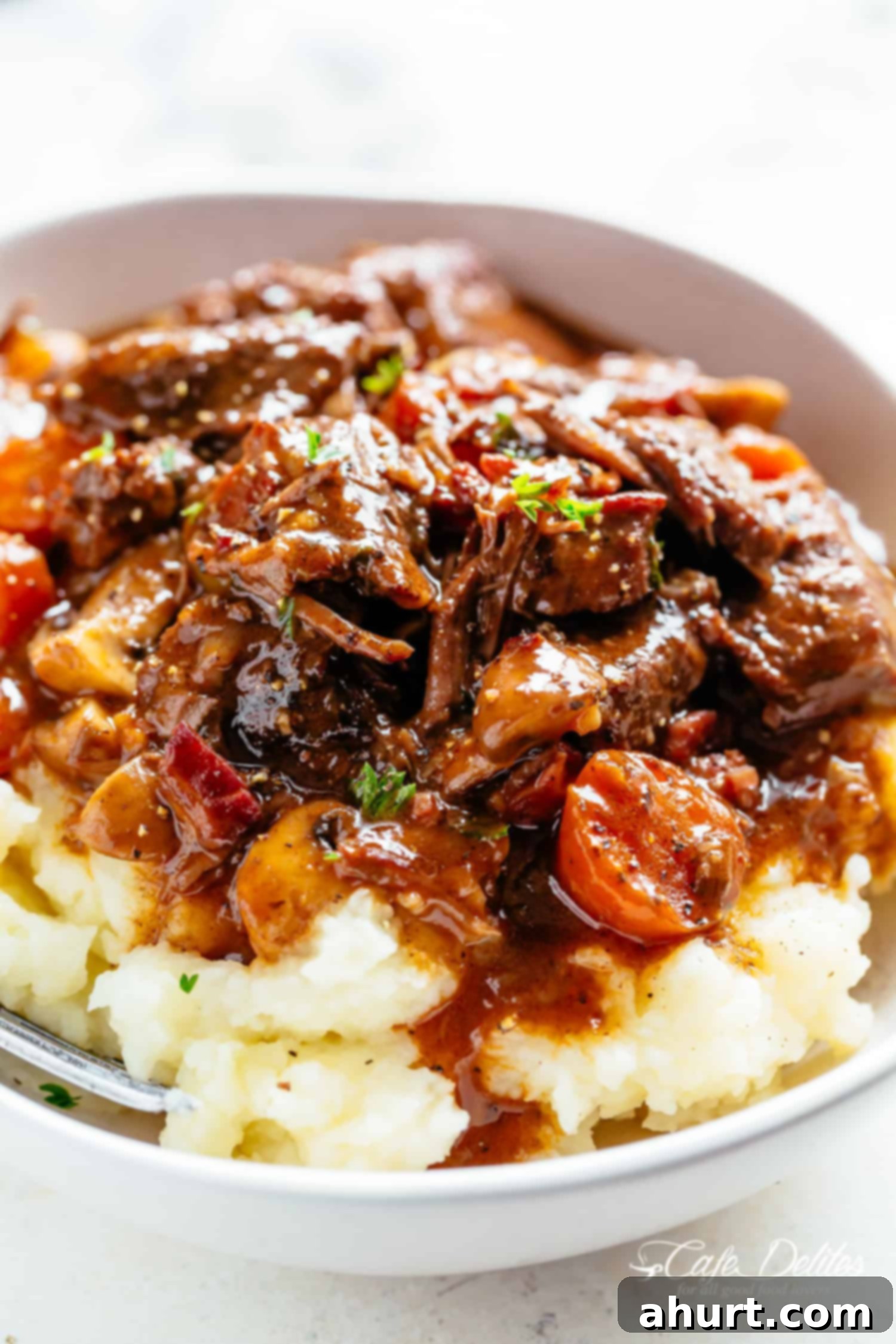 Beef Bourguignon by Julia Child 6 Beef Bourguignon on mashed potatoes with gravy served in a white bowl with a silver fork in a white bowl on a white table