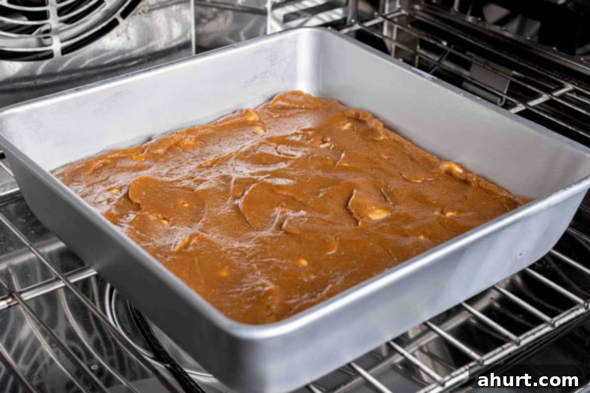 Luxurious White Chocolate Blondie Delights 7 Mixture being poured into a square nonstick baking pan, ready to be placed in the oven.