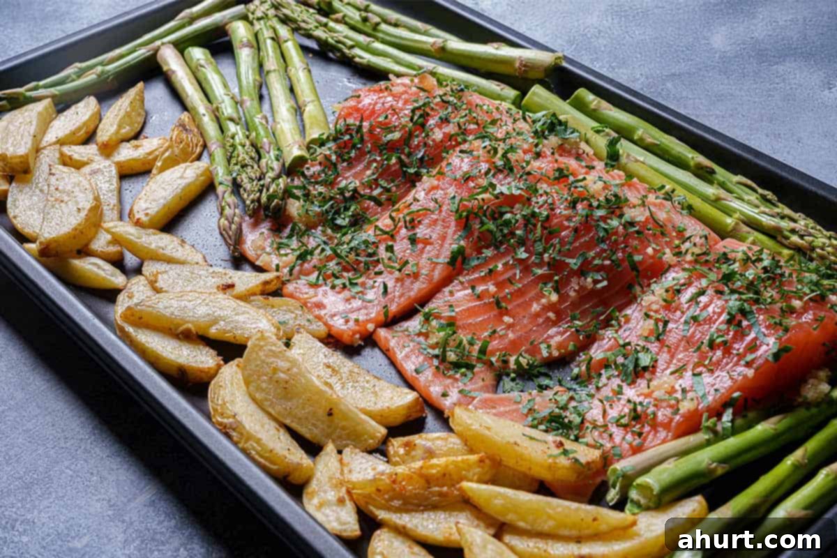 Decadent Garlic Butter Salmon 5 Image of potatoes, asparagus, and salmon being arranged on a baking sheet before being placed into the oven.