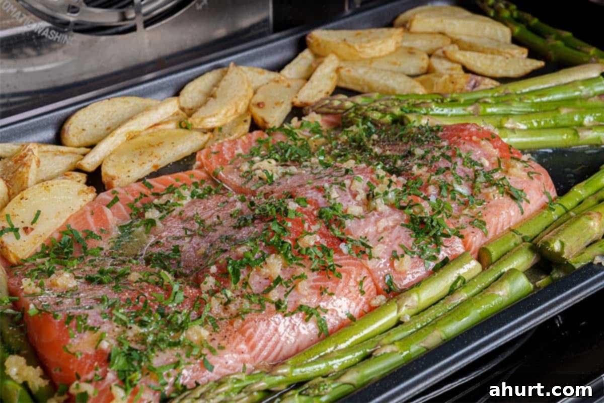 Decadent Garlic Butter Salmon 7 Salmon, potatoes, and asparagus being cooked in the oven until fully cooked through.