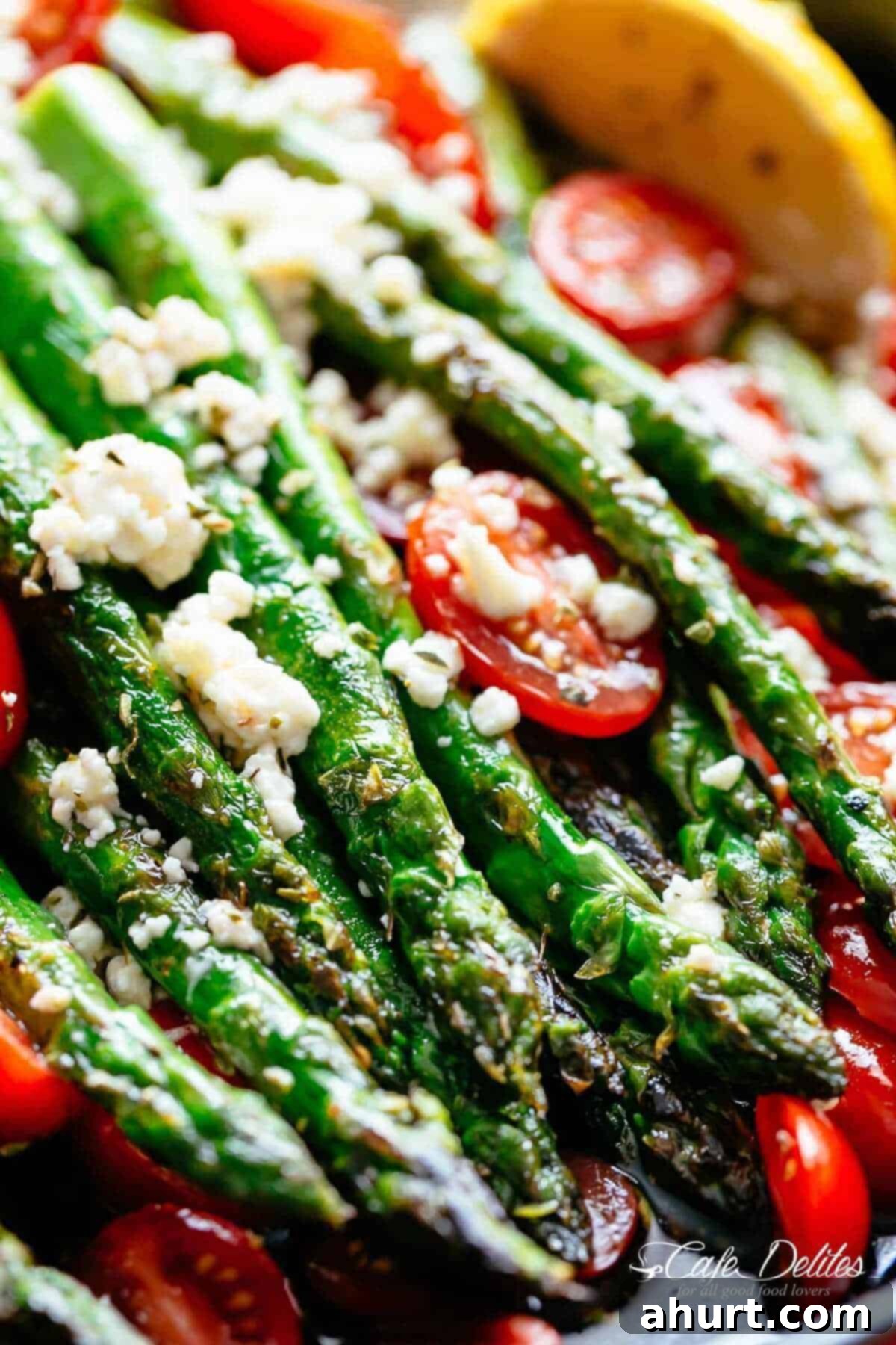 Effortless Lemon Garlic Asparagus 9 close up image of light browned, crunchy asparagi topped with feta cheese and tomatoes.