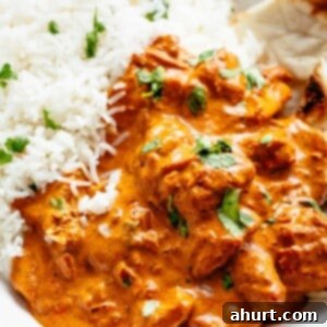 Rich and Creamy Chicken Tikka Masala 11 A close-up shot of Chicken Tikka Masala, generously garnished with fresh coriander, alongside a bed of fluffy white rice and a piece of naan bread. Chunks of chicken, coated in the flavorful sauce, are scattered throughout the dish.