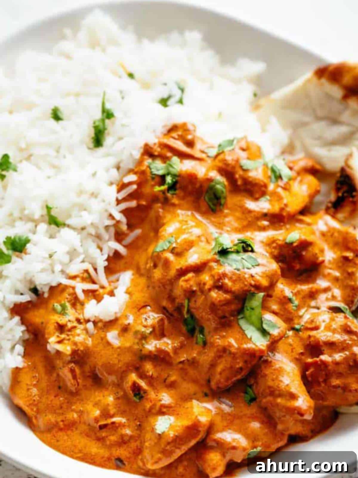 Rich and Creamy Chicken Tikka Masala 10 chicken tikka masala in a bowl garnished with fresh parsley, served beside rice