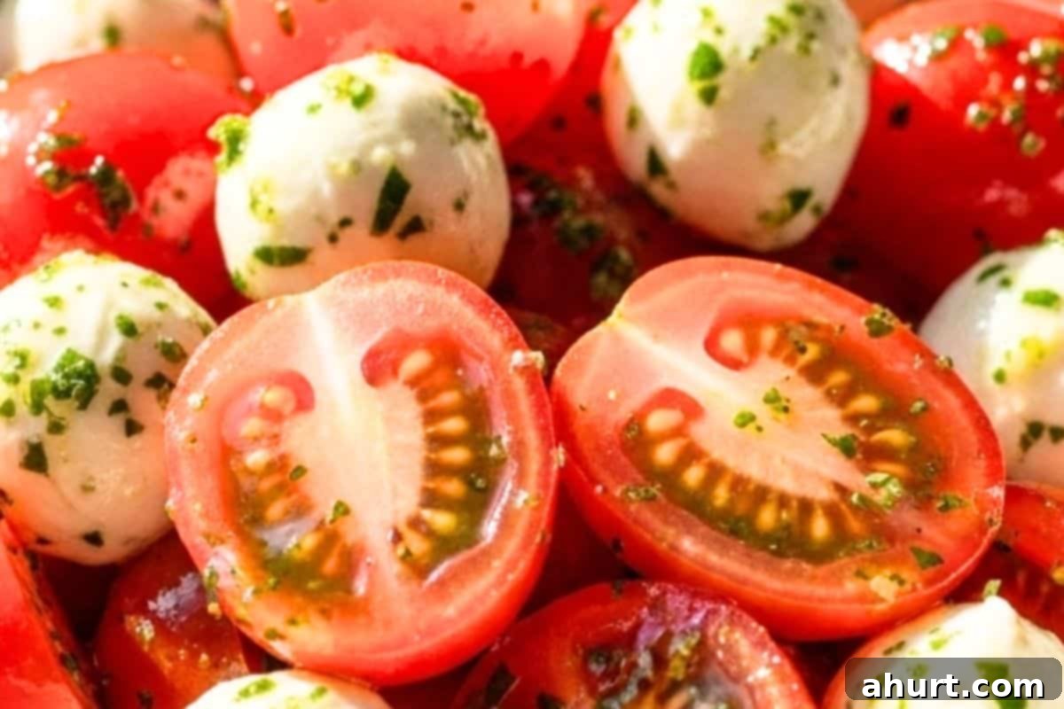 Fresh Caprese Pasta Salad 4 Halved cherry tomatoes and bocconcini mozzarella being added to a bowl with the homemade Italian herb dressing for marination.