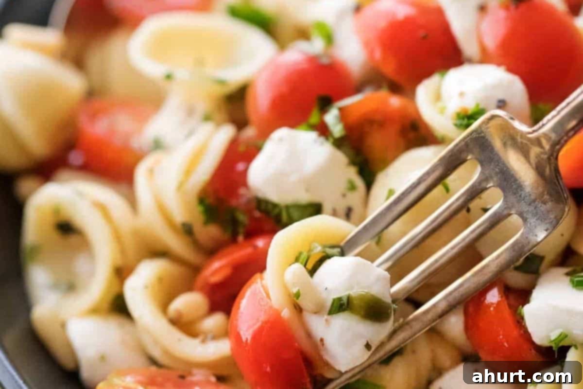 Fresh Caprese Pasta Salad 8 A hand drizzling the reserved dressing over the chilled Caprese pasta salad, garnished with fresh basil and pine nuts, in a large serving bowl.