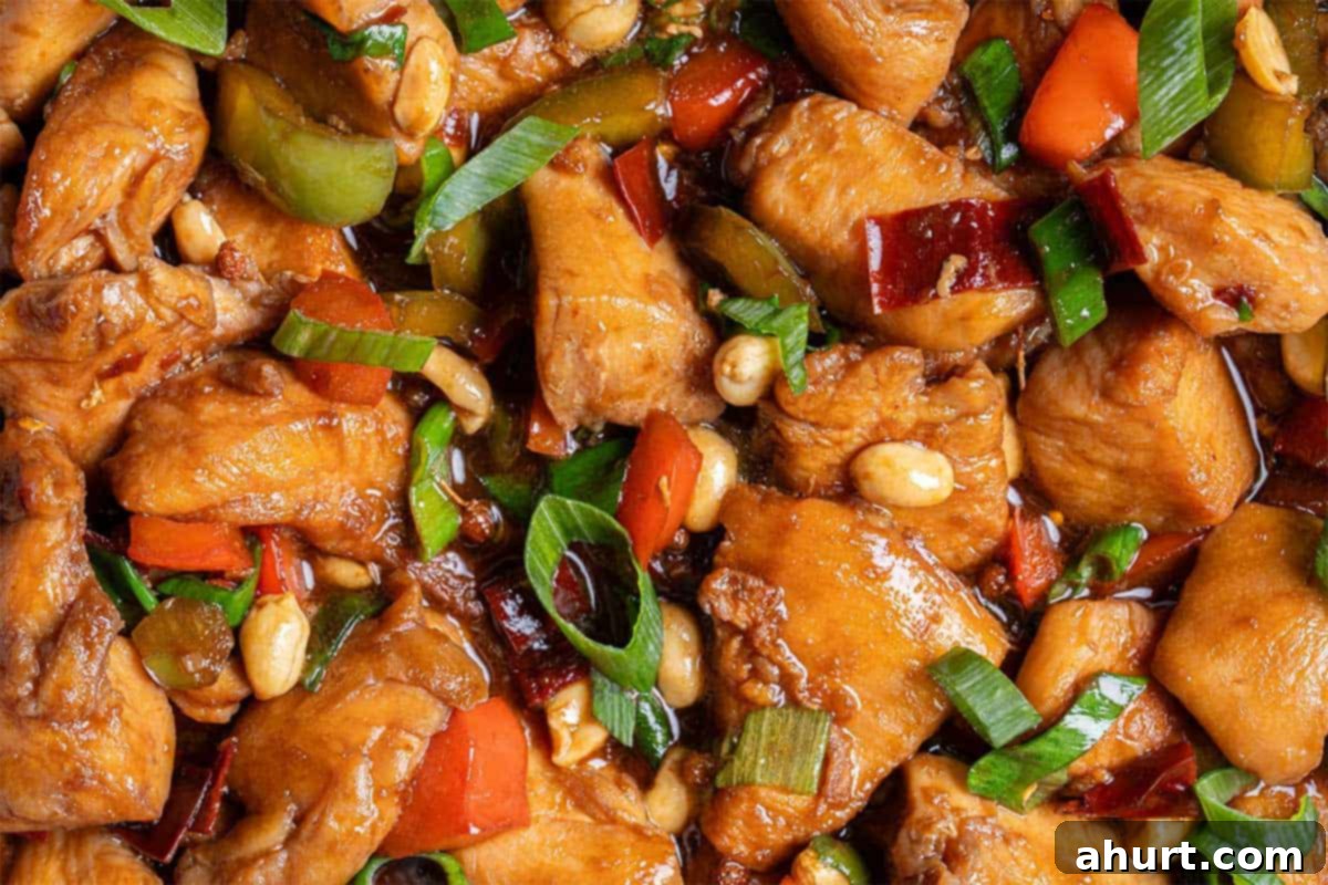 Kung Pao Chicken 10 Close up image of Kung Pao Chicken in a sticky Kung Pao sauce with green and red chopped vegetables picked in with chicken pieces.