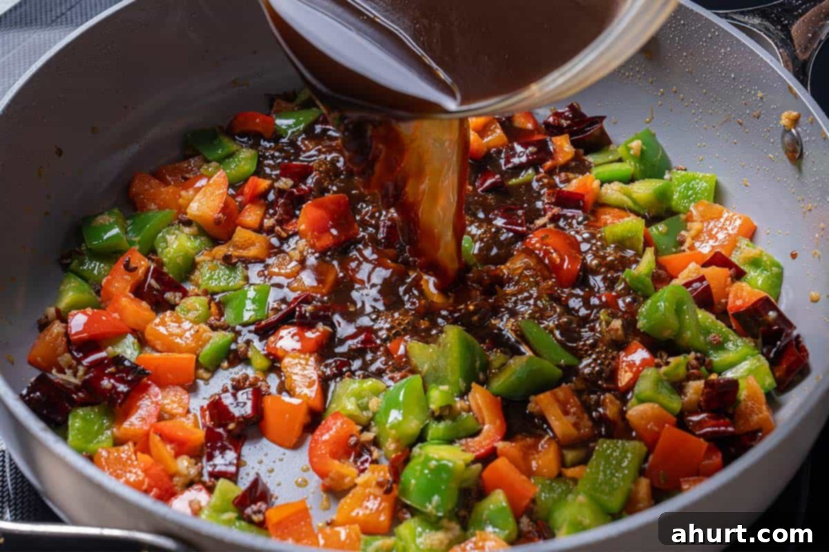Kung Pao Chicken 7 garlic, ginger, chili diced peppers (capsicums) and Sichuan peppercorns with a sauce mixture being poured into the wok