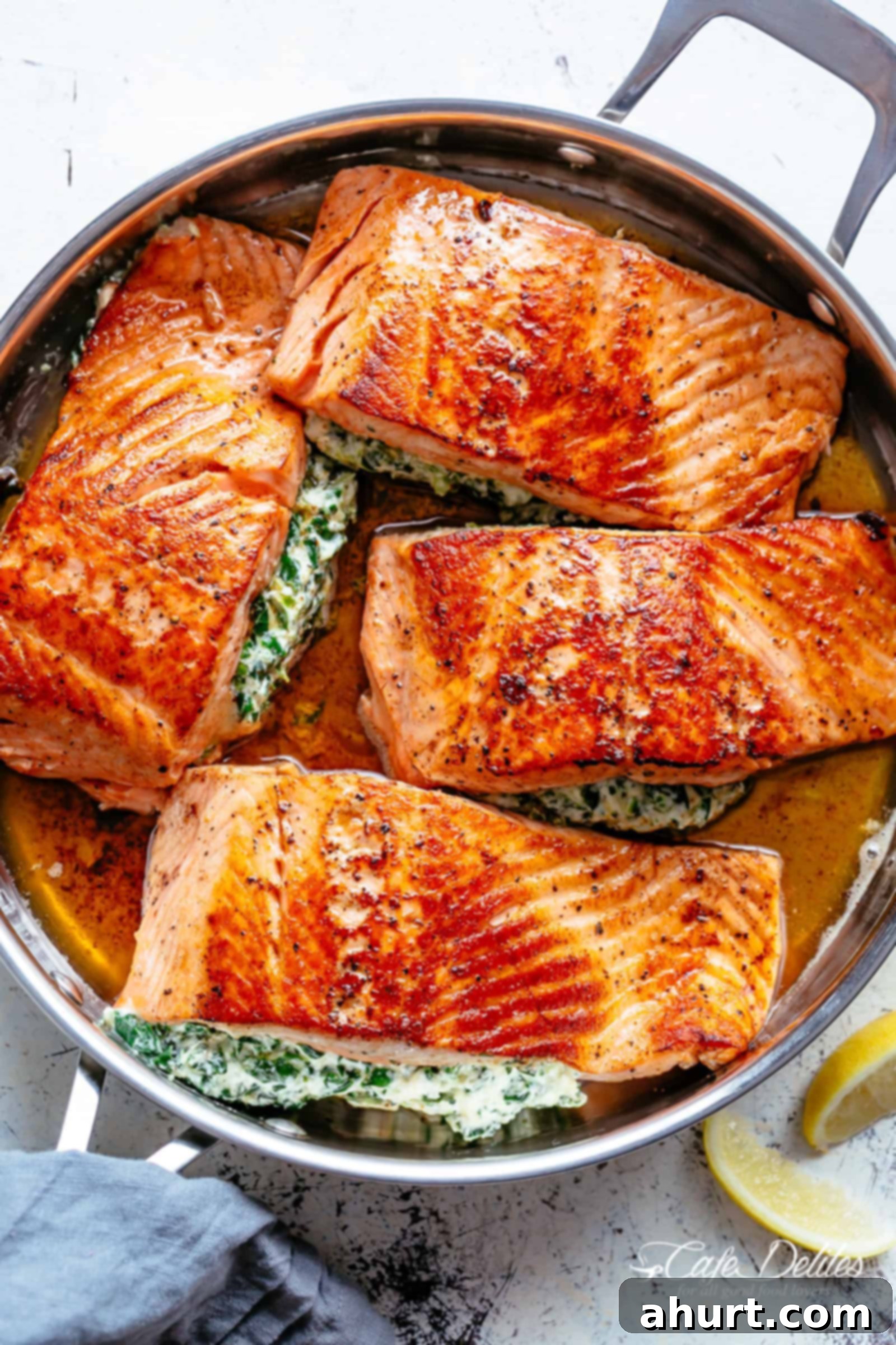 Creamy Spinach Stuffed Salmon in garlic butter includes pan fried AND oven baked methods! | cafedelites.com Four Salmon fillets stuffed with creamed spinach in a garlic butter sauce in a silver frying pan served with lemon wedges on a white table.