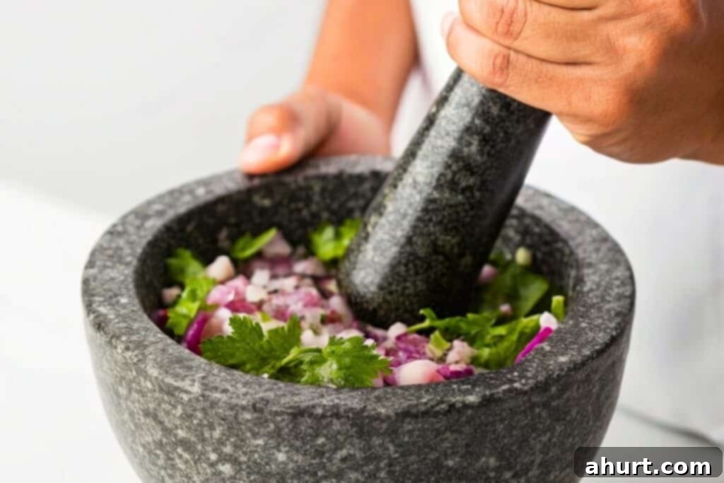 Crafting Irresistible Guacamole 3 Finely chopped red onion, serrano chile, salt, and cilantro being mashed on a cutting board with a fork.
