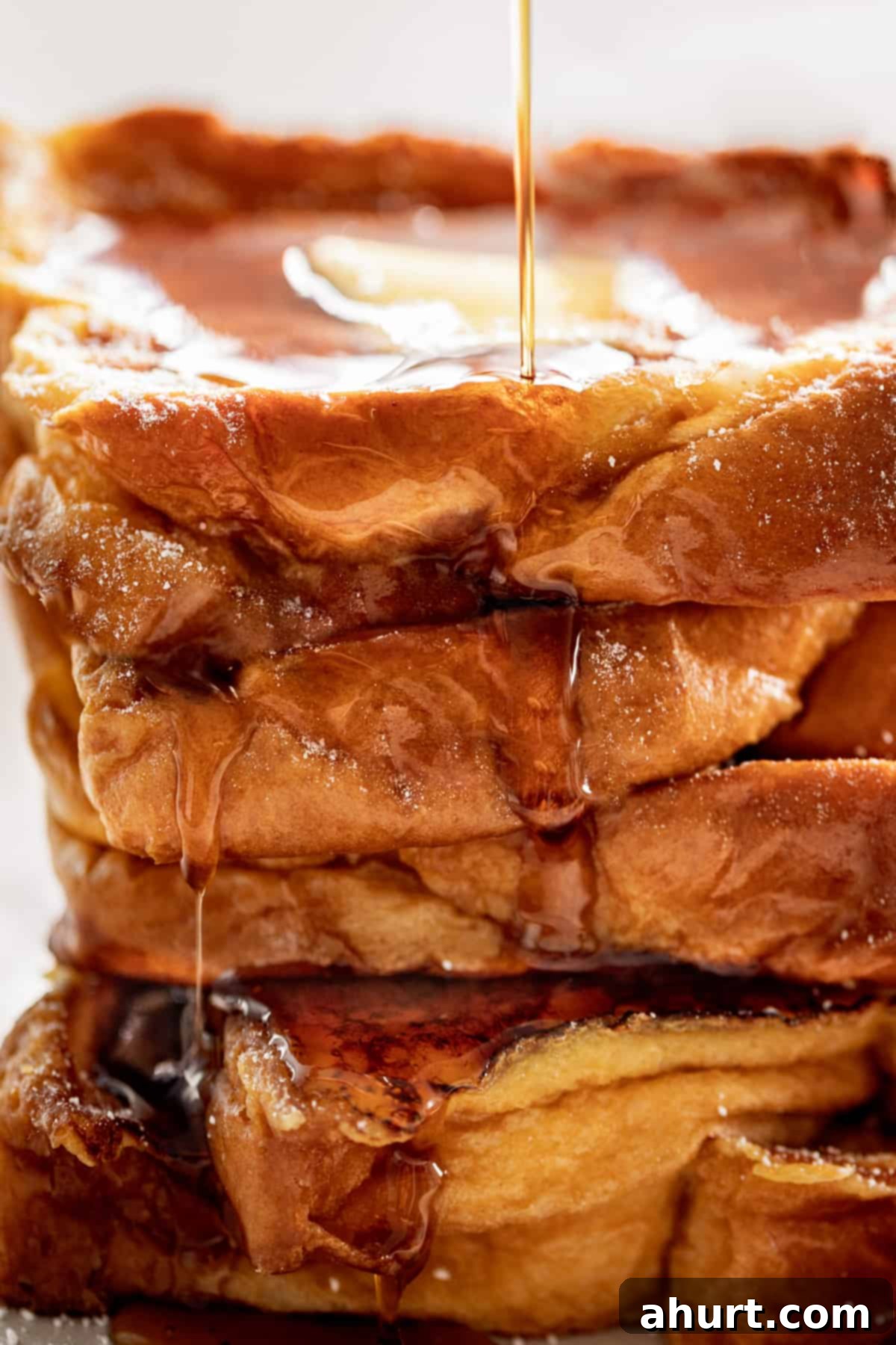 French Toast Perfection 2 Side view image of The Best French Toast drizzled with maple syrup and sprinkled with powdered sugar.
