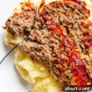 Perfect Homemade Meatloaf 9 Top view image of A fork slicing through a piece of meatloaf and mashed potato on a white plate.