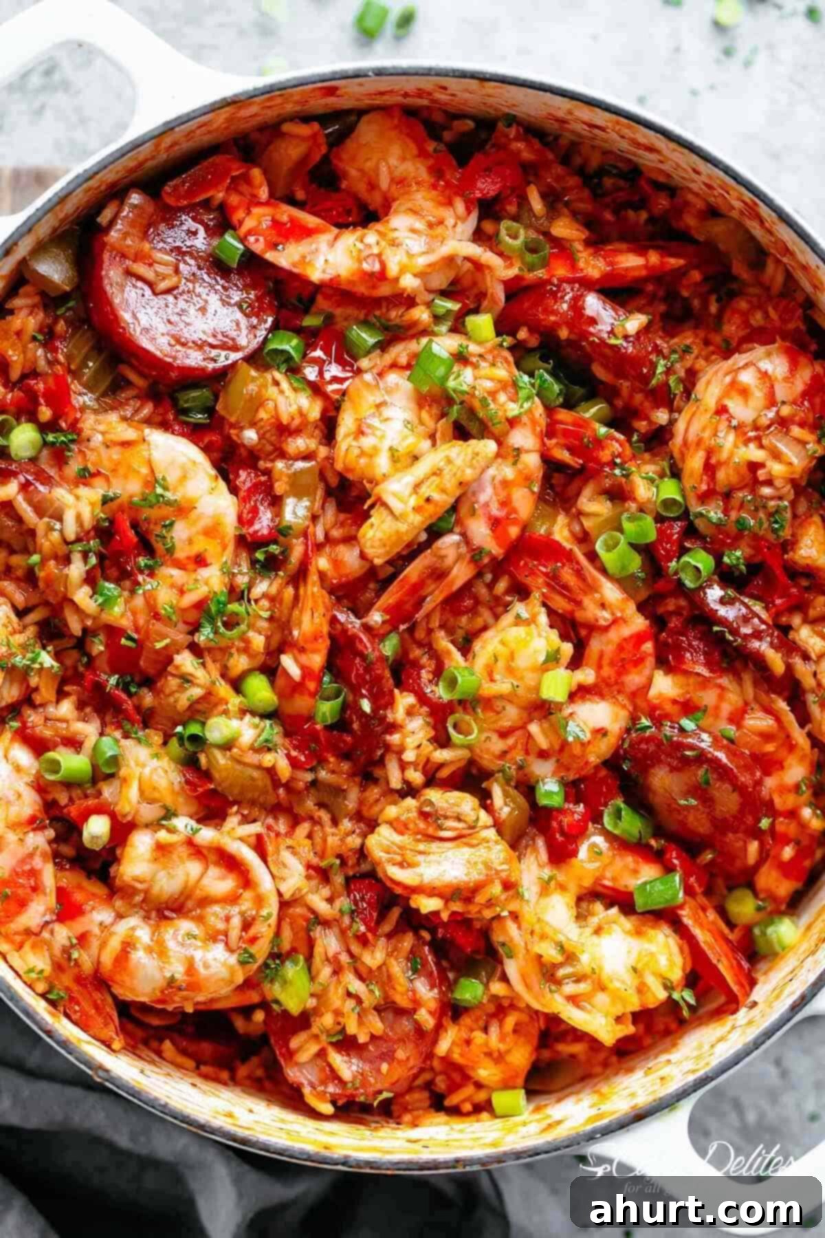 An authentic Creole Jambalaya recipe! | cafedelites.com Close-up image of a colorful, freshly prepared jambalaya with shrimp and sausage, cooked in a white pot, ready to be served.