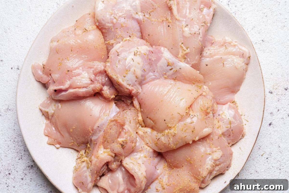 Creamy Mushroom Garlic Chicken Thighs 5 chicken sits on a white plate being coated with a seasoning