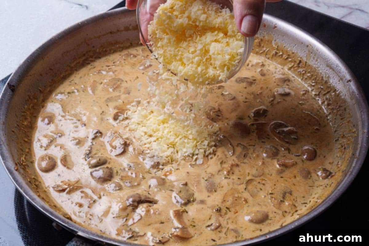 Creamy Mushroom Garlic Chicken Thighs 8 parmesan cheese is poured into a creamy mushroom sauce over a stove in a pan