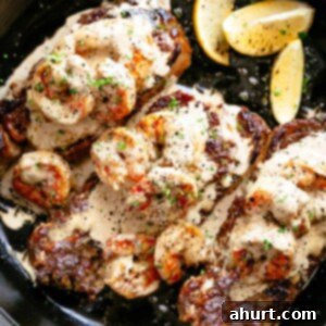 Land and Sea Feast 3 Three pieces of cooked steak in a pan with prawns laid on top and covered in creamy garlic sauce.