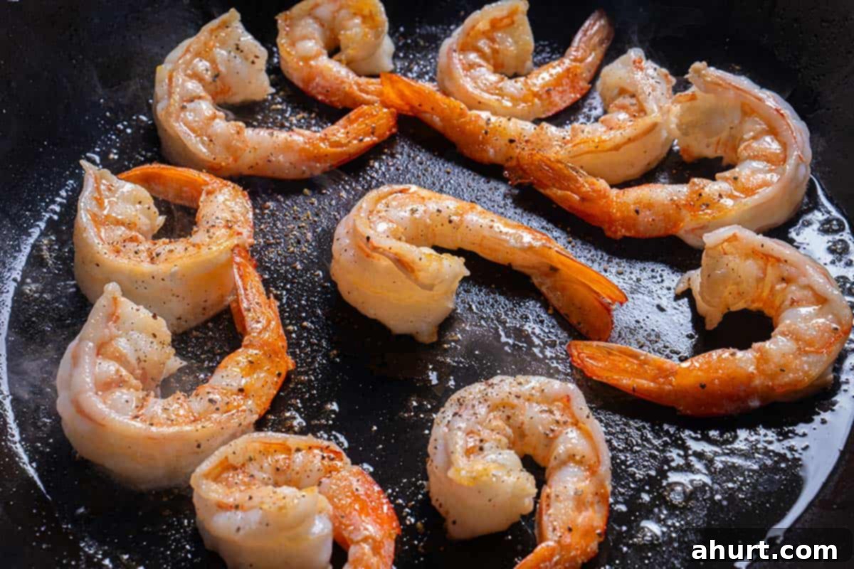 Luscious Low Carb Creamy Garlic Parmesan Shrimp 3 A close-up image of shrimp being heated in a large skillet over medium-high heat.