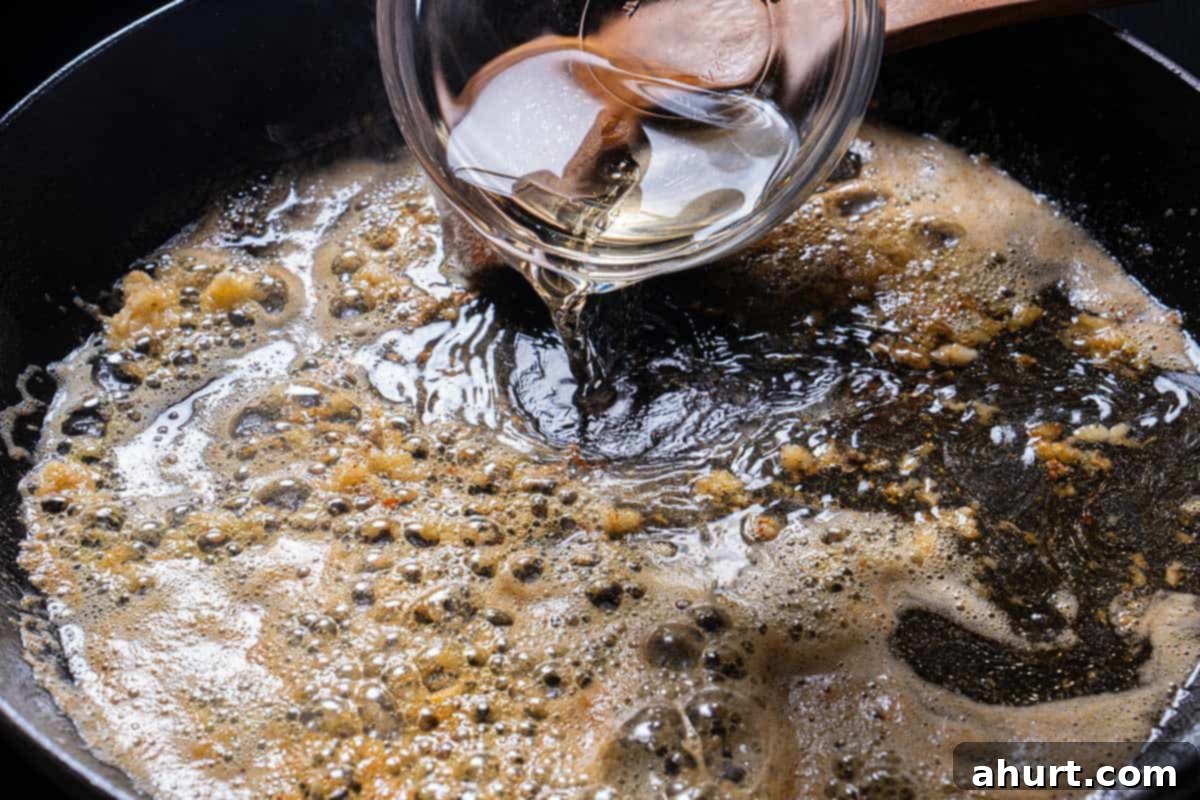 Luscious Low Carb Creamy Garlic Parmesan Shrimp 4 An image of white wine being added to the skillet where garlic is being sautéed together with butter.