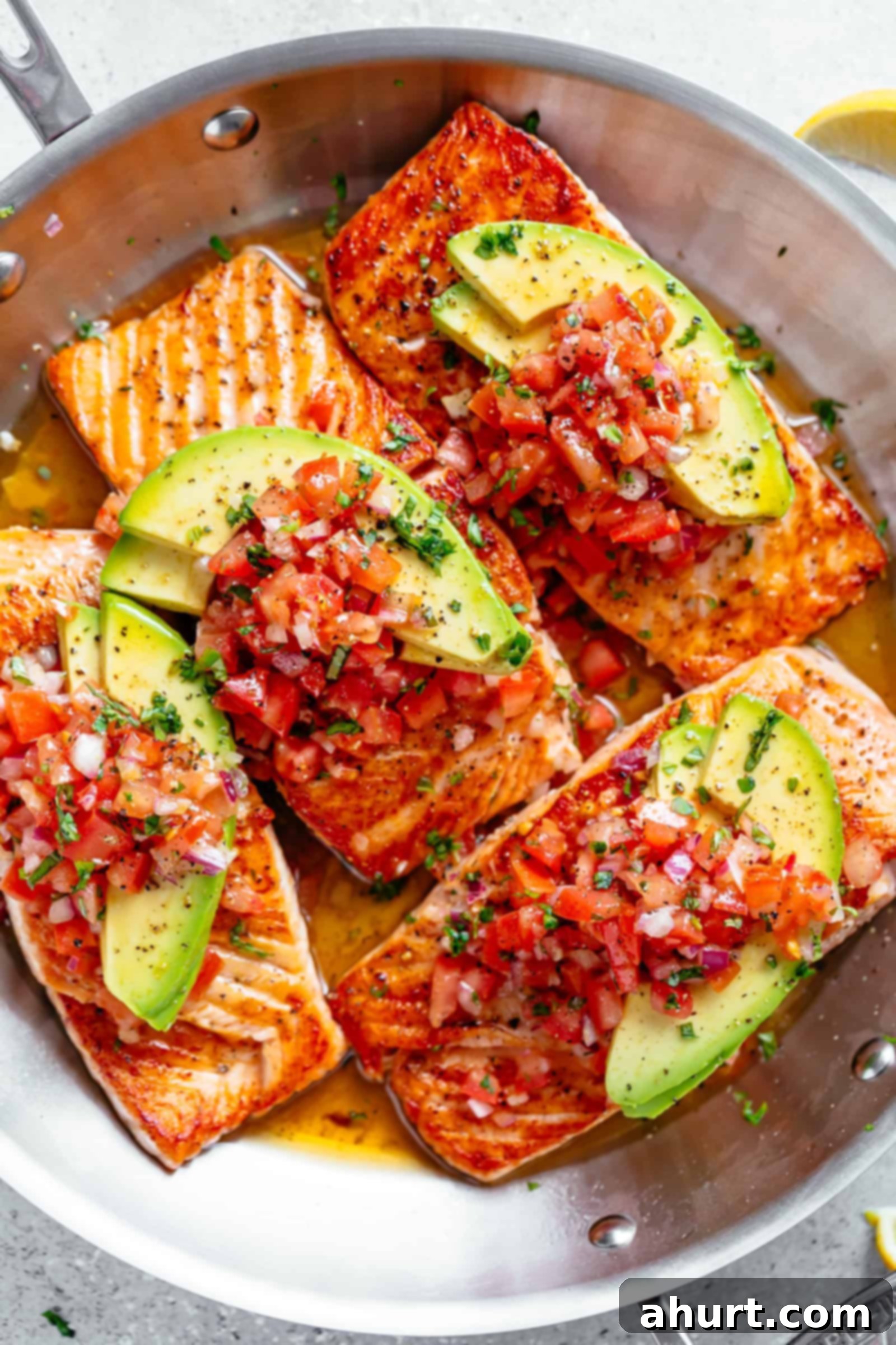 Four pieces of golden pan-seared salmon in a buttery garlic lemon sauce, generously topped with a fresh tomato salsa and ripe avocado slices.