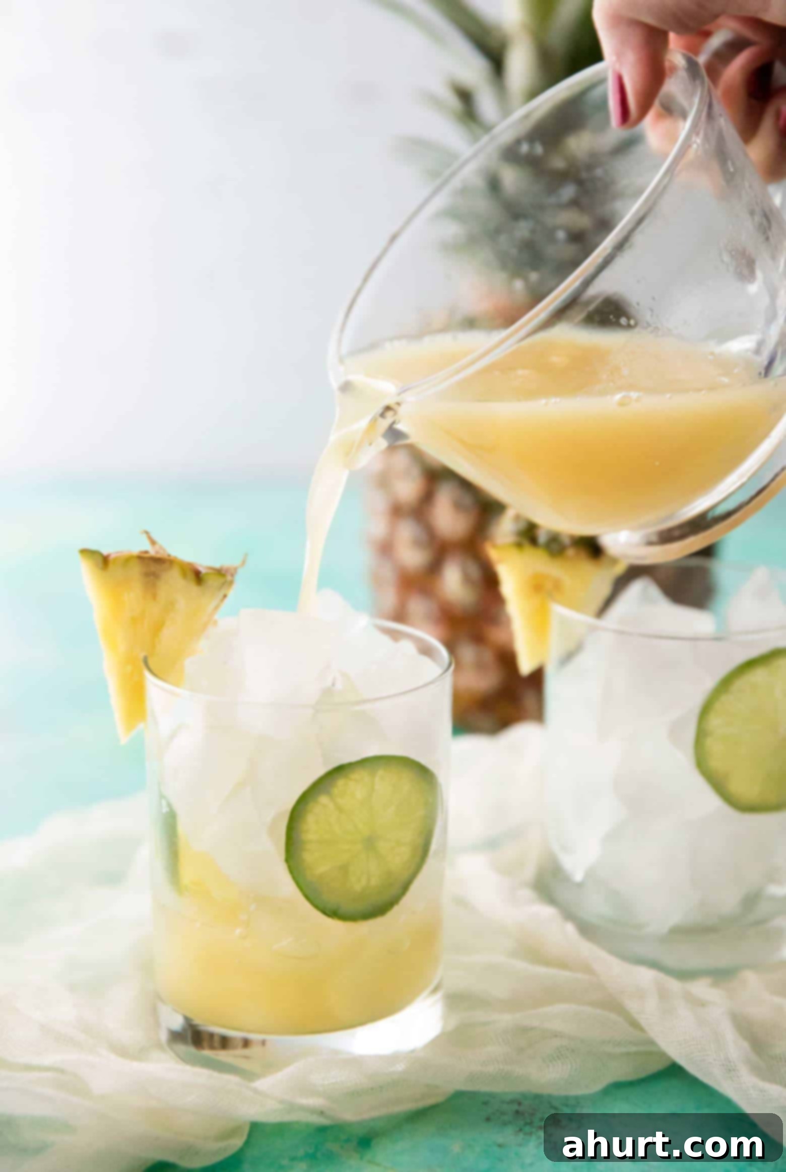Cocktails | cafedelites.com Tropical Pineapple Rum Punch being poured into a glass full of ice, showcasing its golden color and inviting texture.
